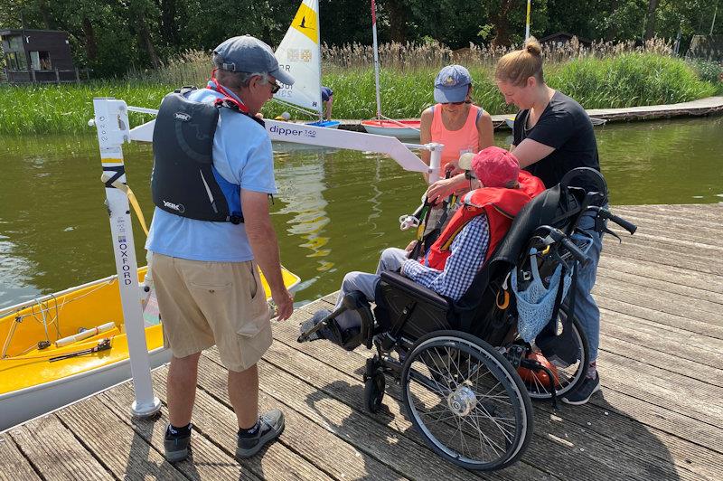 Hoist process step 1 - the sailor has arrived already sitting on the sling (see black fabric hanging over back of wheelchair) and the spreader bar can be attached - photo © Magnus Smith